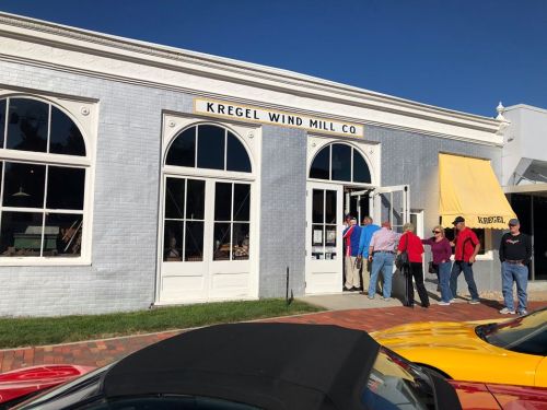 A group of people stands outside the Kregel Wind Mill Company building, featuring large windows and a yellow awning.