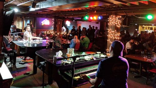 A lively bar scene with a pianist performing on stage, surrounded by a crowded audience enjoying the music.