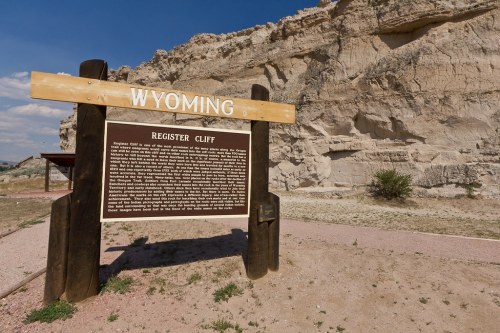 Sign for Register Cliff in Wyoming, featuring historical information against a backdrop of rocky cliffs and blue sky.