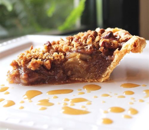 A slice of pie with a crumbly topping on a white plate, drizzled with caramel sauce.