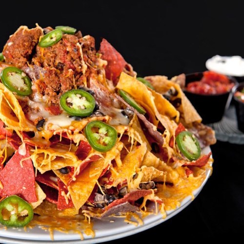 A colorful plate of nachos topped with cheese, jalapeños, ground meat, and served with salsa and sour cream on the side.