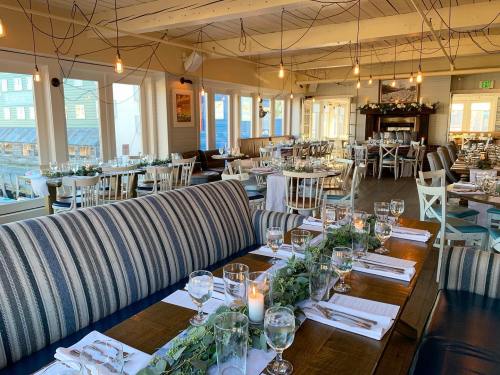 A cozy restaurant interior with tables set for dining, featuring greenery, candles, and warm lighting.