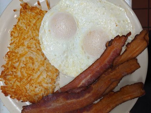 A plate with two sunny-side-up eggs, crispy bacon strips, and golden hash browns.