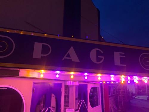 A brightly lit sign reading "PAGE" on a building at dusk, with colorful lights illuminating the entrance.
