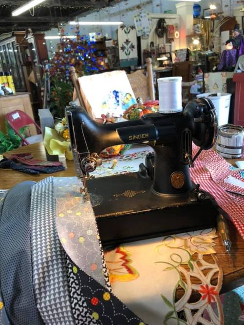 A vintage Singer sewing machine on a table, surrounded by colorful fabrics and craft items in a cozy shop setting.