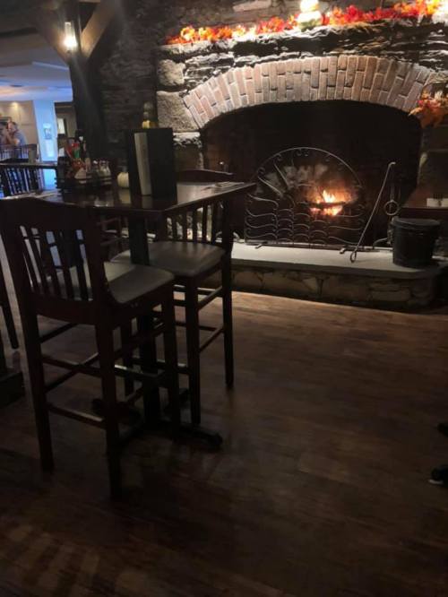 Cozy interior with a brick fireplace, wooden bar stools, and autumn decorations above the mantel. Warm ambiance.