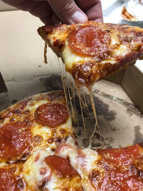 A hand lifts a slice of pepperoni pizza, showcasing melted cheese and a crispy crust from a pizza box.