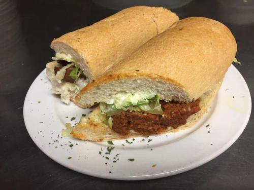 A sandwich on a plate, filled with shredded meat, lettuce, and mayonnaise, served on a toasted hoagie roll.