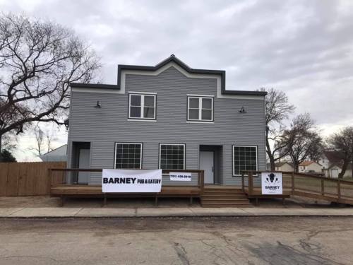 Exterior of a two-story building with a wooden deck, featuring signs for "Barney Pub & Eatery." Cloudy sky in the background.