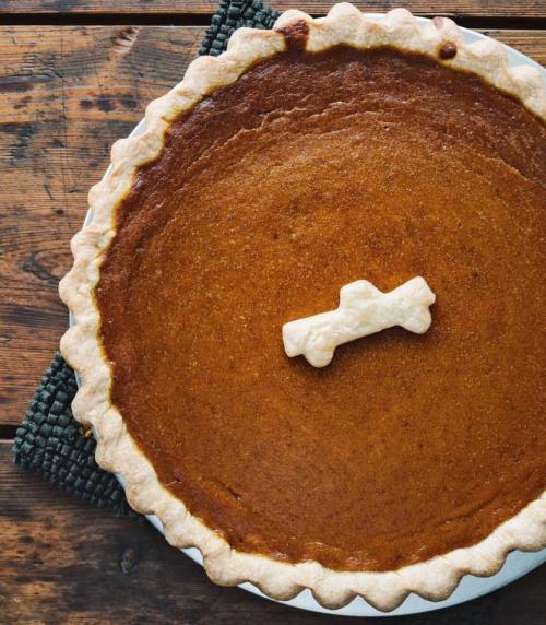 A freshly baked pumpkin pie with a golden crust and a decorative pastry cross on top, resting on a wooden table.