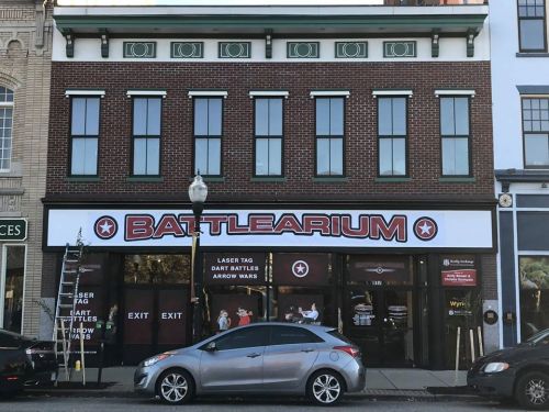 Exterior of a building with a sign reading "BATTLEARIUM," featuring laser tag, dart battles, and arrow wars.
