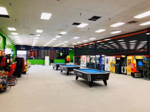 A spacious arcade with pool tables, arcade machines, and vending machines in a brightly lit room.