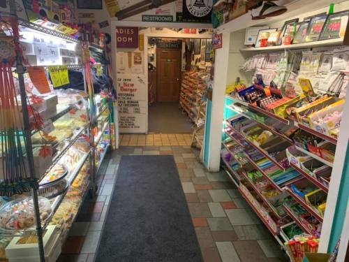 A cozy shop interior with shelves of snacks and candy, leading to a restroom and seating area.