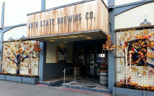 Entrance of 49th State Brewing Co., decorated with autumn leaves and pumpkins, featuring a wooden sign above the door.