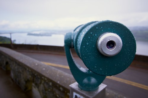 A wet telescope overlooks a scenic view of a river and landscape, with raindrops on its surface.