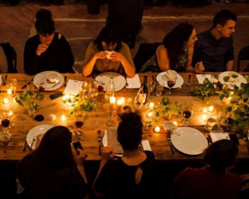 A dimly lit dinner table set with plates, wine glasses, and candles, with guests engaged in conversation.
