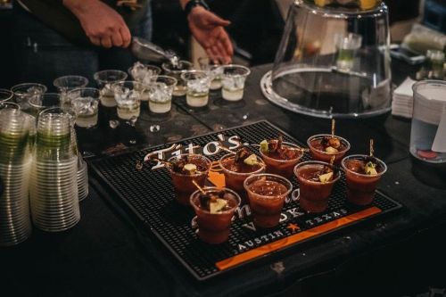 A bar setup featuring cups of cocktails and a bartender preparing drinks in a lively atmosphere.