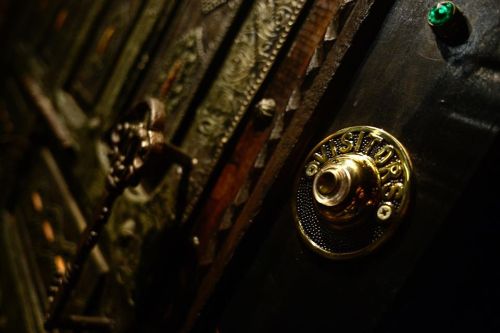 Close-up of an ornate door with a brass doorbell labeled "VISITORS" and intricate metalwork in the background.
