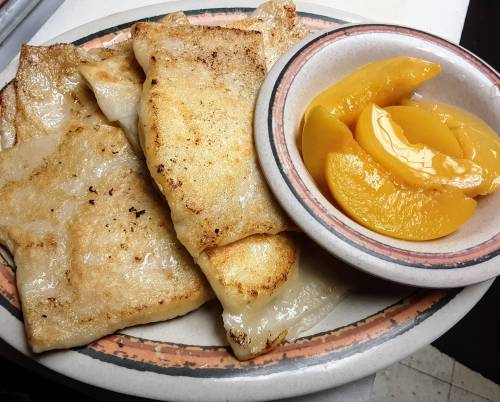 A plate of golden-brown fried dumplings served with a side of sliced peaches in syrup.