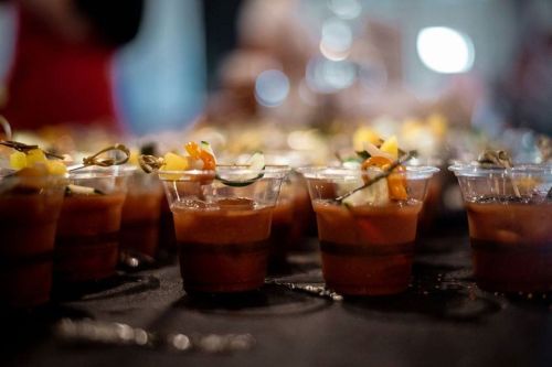 A close-up of small cups filled with a colorful, layered drink garnished with vegetables and herbs.