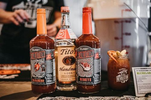 Three bottles of Bloody Revolution mix, including Habanero and Ribeye, alongside a bottle of Tito's Handmade Vodka.