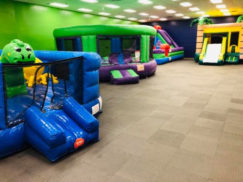 A colorful indoor play area featuring various inflatable bounce houses and slides on a carpeted floor.
