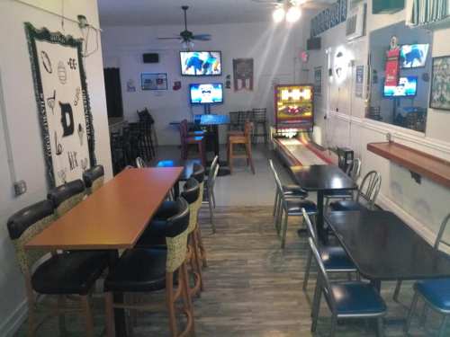 Interior of a casual bar with tables, chairs, and TVs, featuring a jukebox and a bowling lane in the background.