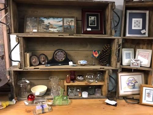 A rustic wooden shelf displays various vintage items, including framed pictures, glassware, and decorative objects.