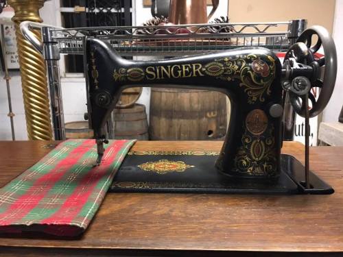 A vintage Singer sewing machine on a wooden table, with a plaid fabric piece beside it.