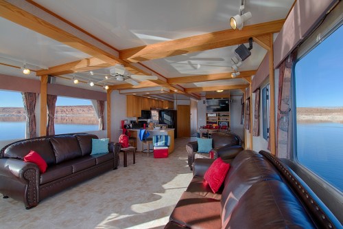 Spacious living area with leather sofas, wooden beams, and large windows overlooking a serene lake view.