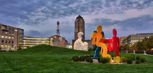 Colorful sculptures in a grassy park with a city skyline and cloudy sky in the background.