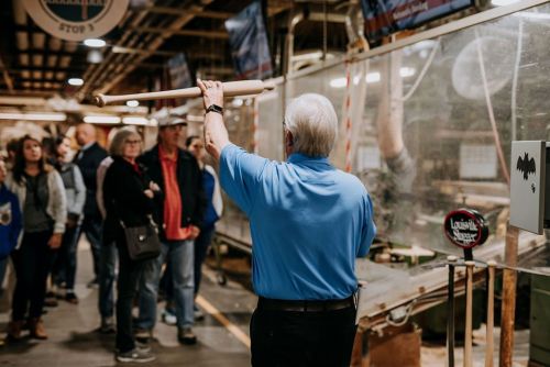 A man in a blue shirt demonstrates with a bat to an audience in a wildlife exhibit.