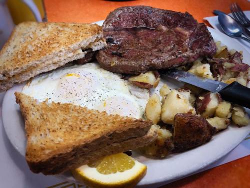 A hearty breakfast plate featuring steak, eggs, toast, and seasoned potatoes, garnished with a slice of lemon.