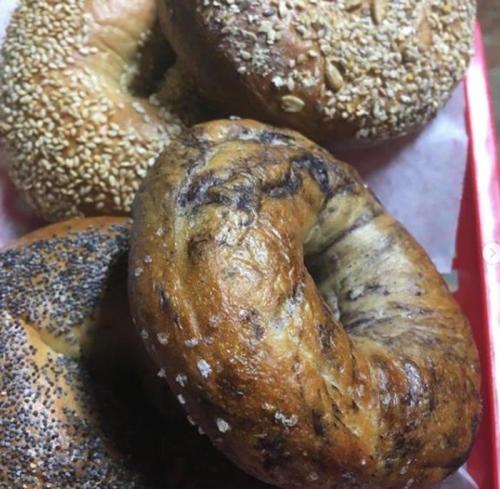 A close-up of assorted bagels, including sesame, poppy seed, and a marbled variety, arranged on a red tray.