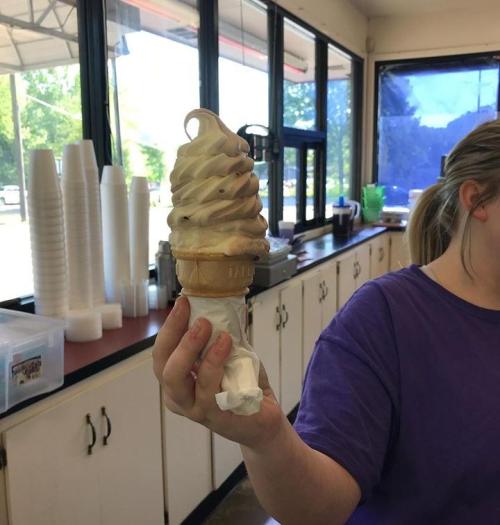 A person holds a soft-serve ice cream cone with swirled chocolate and vanilla in a shop with a bright interior.