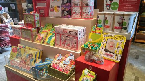 A colorful display of classic toys and games, including board games, puzzles, and novelty items on a red shelf.