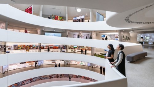 Two visitors admire exhibits in a modern, spiraling art gallery with various displays on the walls.