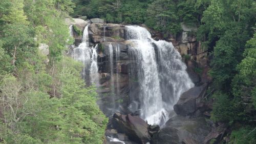 A cascading waterfall surrounded by lush green trees and rocky terrain.