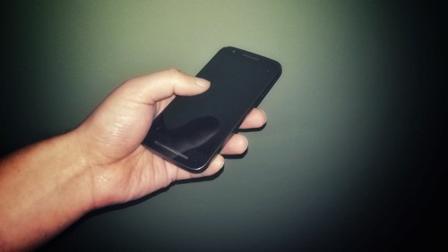 A hand holding a black smartphone against a plain green background.