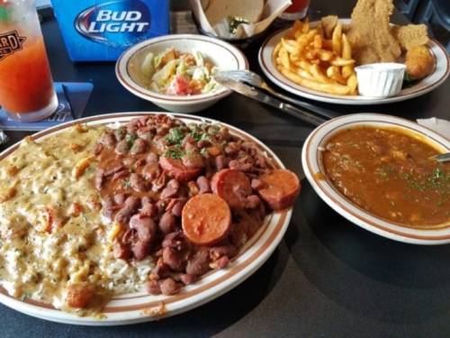 A table with a variety of dishes: rice with sausage and beans, gumbo, salad, fries, and a drink.