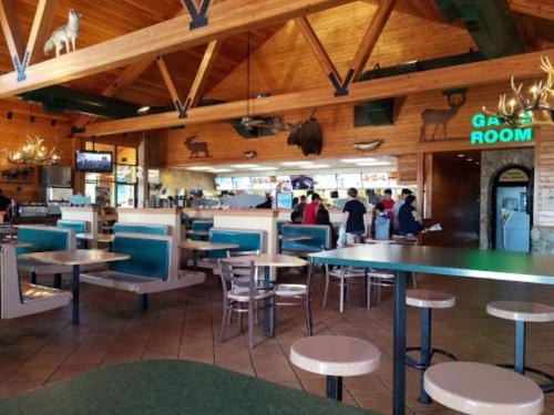 Interior of a rustic restaurant with wooden beams, animal decor, and a dining area with tables and a counter in the background.