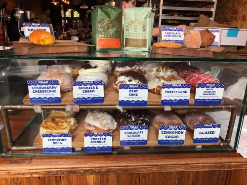 A display case filled with various donuts, labeled with flavors like strawberry cheesecake, coffee cake, and glazed.