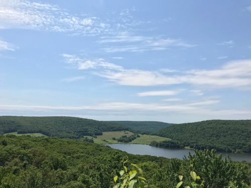 A scenic view of a lush green landscape with rolling hills and a calm lake under a blue sky with scattered clouds.