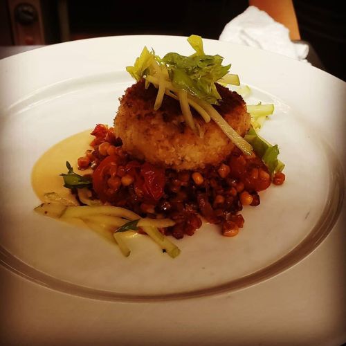 A plated dish featuring a crispy cake atop a colorful mix of vegetables and sauce, garnished with green onions.