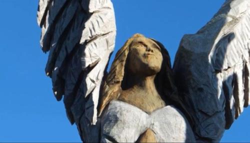 A wooden sculpture of an angel with outstretched wings against a clear blue sky.
