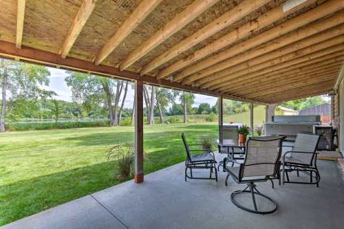 A covered patio with a table and chairs, overlooking a grassy yard and trees in the background.