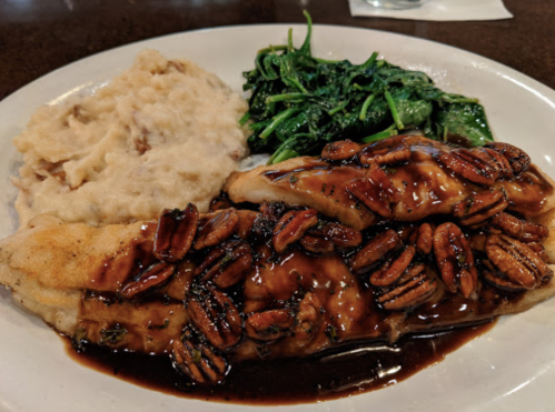 A plate featuring fish topped with pecans, served with creamy mashed potatoes and sautéed greens.
