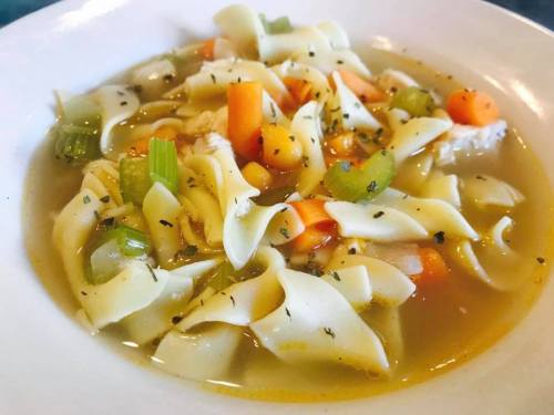 A bowl of chicken noodle soup with pasta, carrots, celery, and herbs in a savory broth.