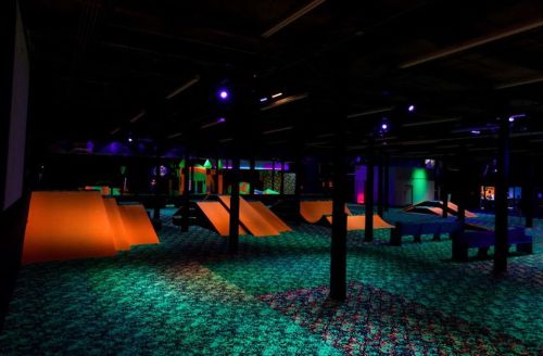 A dimly lit indoor skate park with colorful ramps and glowing lights on a patterned floor.