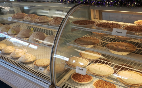 A display case filled with various pies, including pecan and lemon, neatly arranged on shelves.